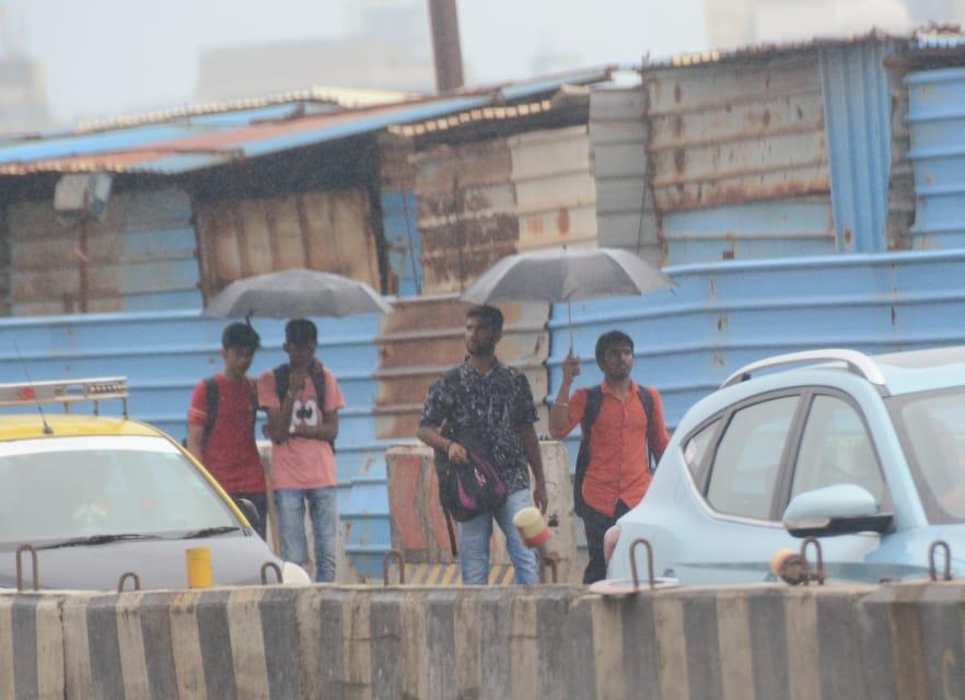 Pedestrians holding umbrellas walk at Marine Drive during rainfall.