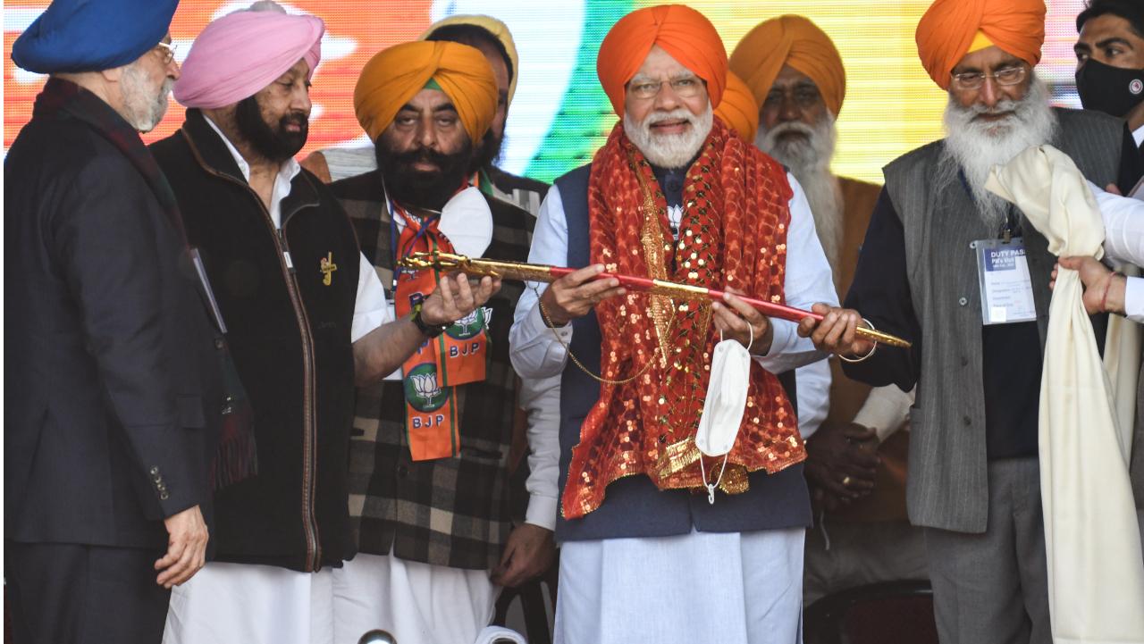 Indian Prime Minister Narendra Modi (centre) wears a traditional turban and holds a sword presented by Union Minister Hardeep Singh Puri (L), Punjab Lok Congress leader and former Punjab Chief Minister Captain Amarinder Singh (2L) and Member of Rajya Sabha Sukhdev Singh Dhindsa (R), during an election rally for the upcoming Punjab state assembly elections, in Jalandhar on February 14, 2022. Photo Courtesy: AFP