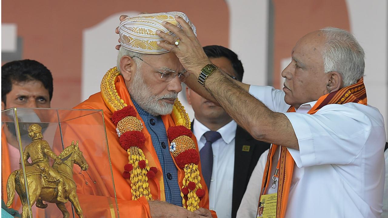 Karnataka state BJP leader B.S. Yeddyurappa (right) puts a traditional turban on Indian Prime Minister Narendra Modi during a gathering 'Parivarthana Rally' in Bangalore on February 4, 2018. Photo Courtesy: AFP