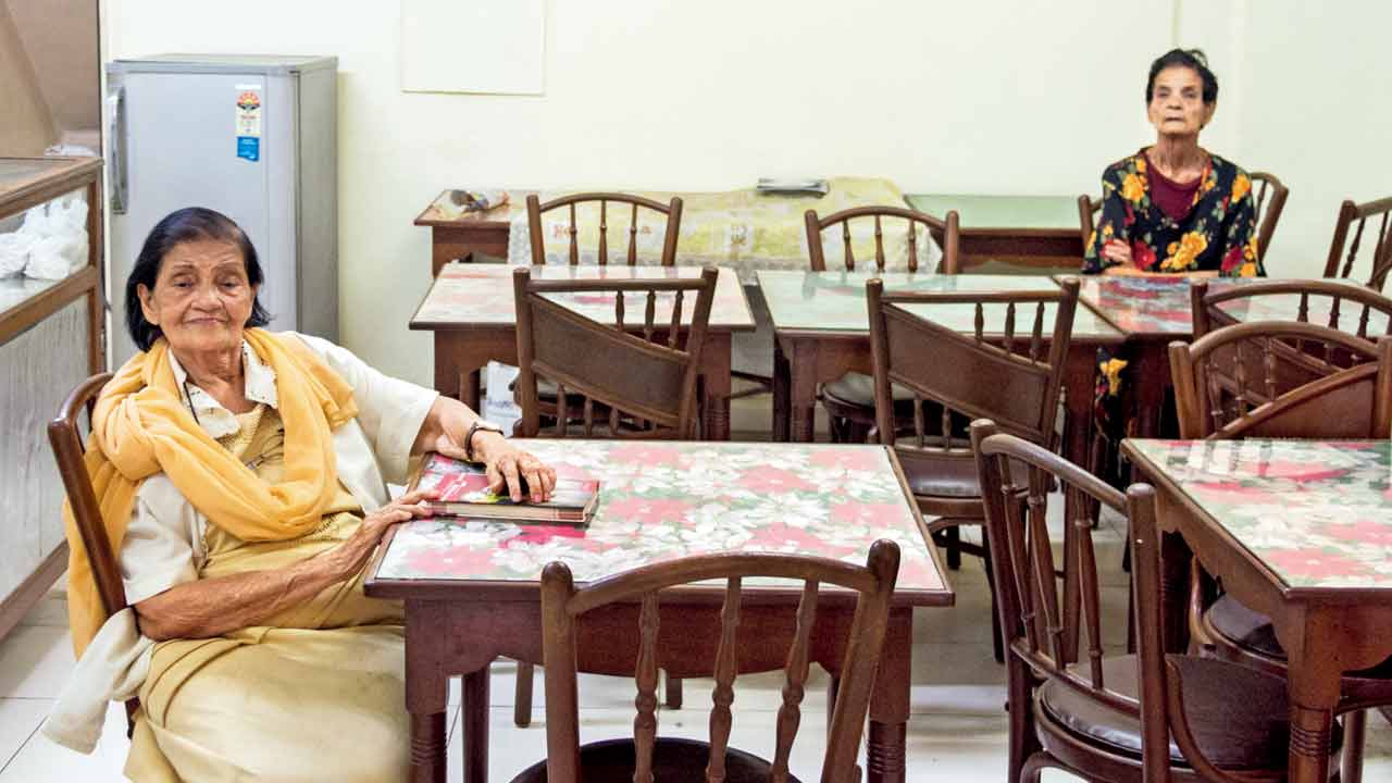 In this file photo, Philomena D’Souza, who died at age 85 in April 2020, is seen at C D’Souza in the company of her friend Bella Athavle, who sat on a separate table and watched the world go by the gully. IMAGE COURTESY/Bombaywalla Historical Works; Hashim Badani