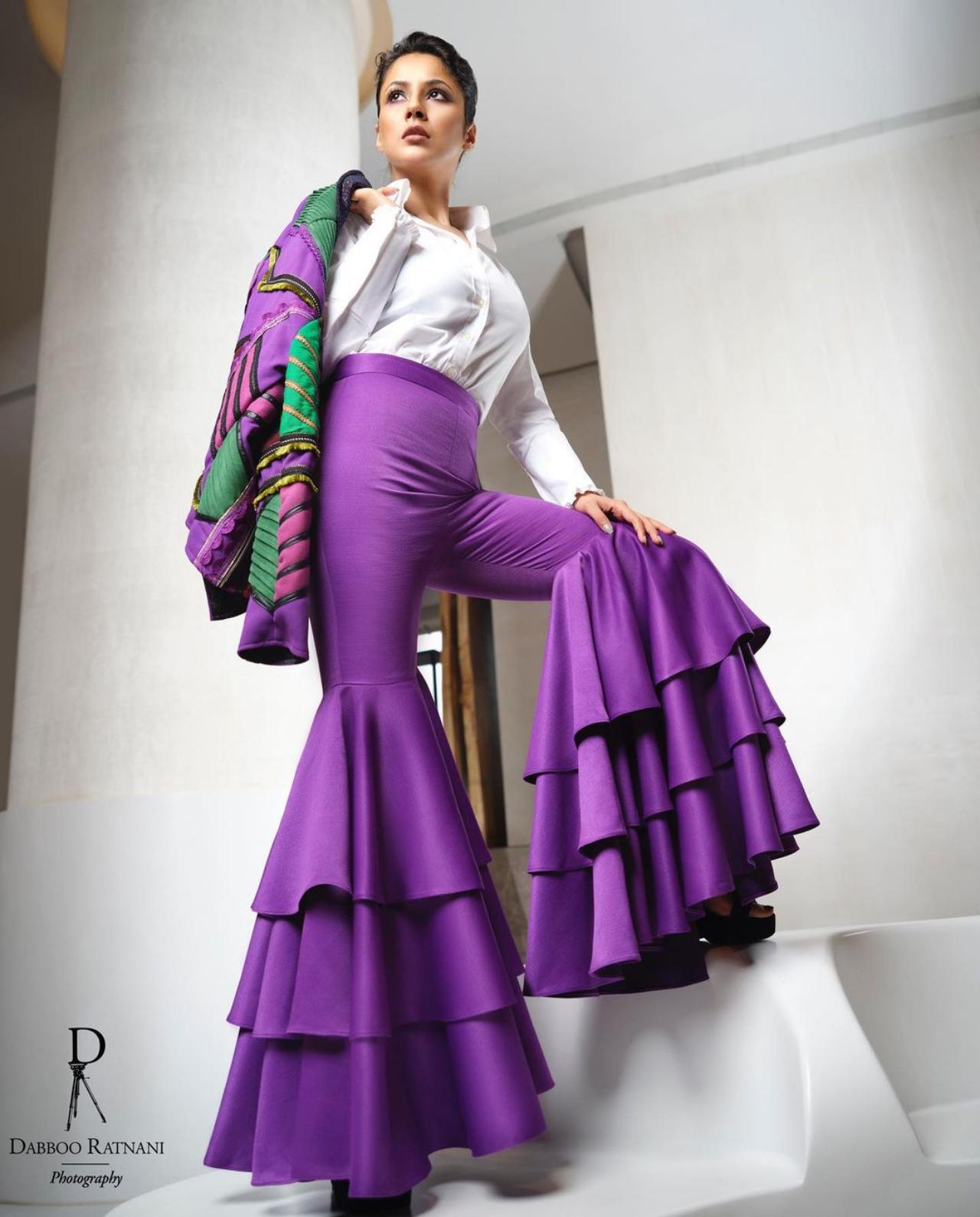 Shehnaaz really does not shy away from bright colours! Gill can be seen donning a pair of bright purple flared pants, an emerald green and purple jacket and a white shirt to bring the look together. The photo was clicked by celebrity photographer Daboo Ratnani.