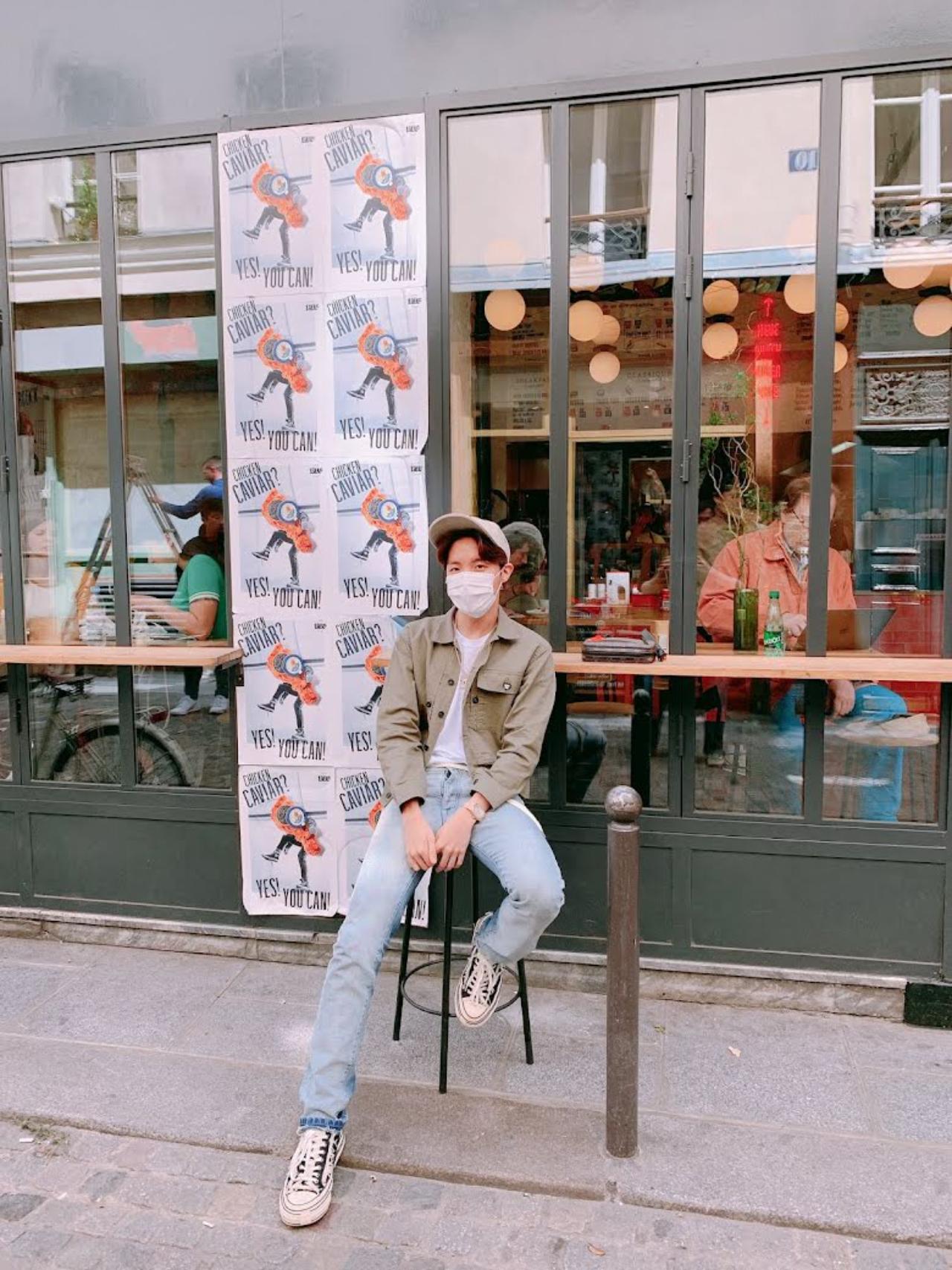 J-Hope proves simple is best in a pair of jeans and an olive green jacket while enjoying a summer evening at a Parisian cafe