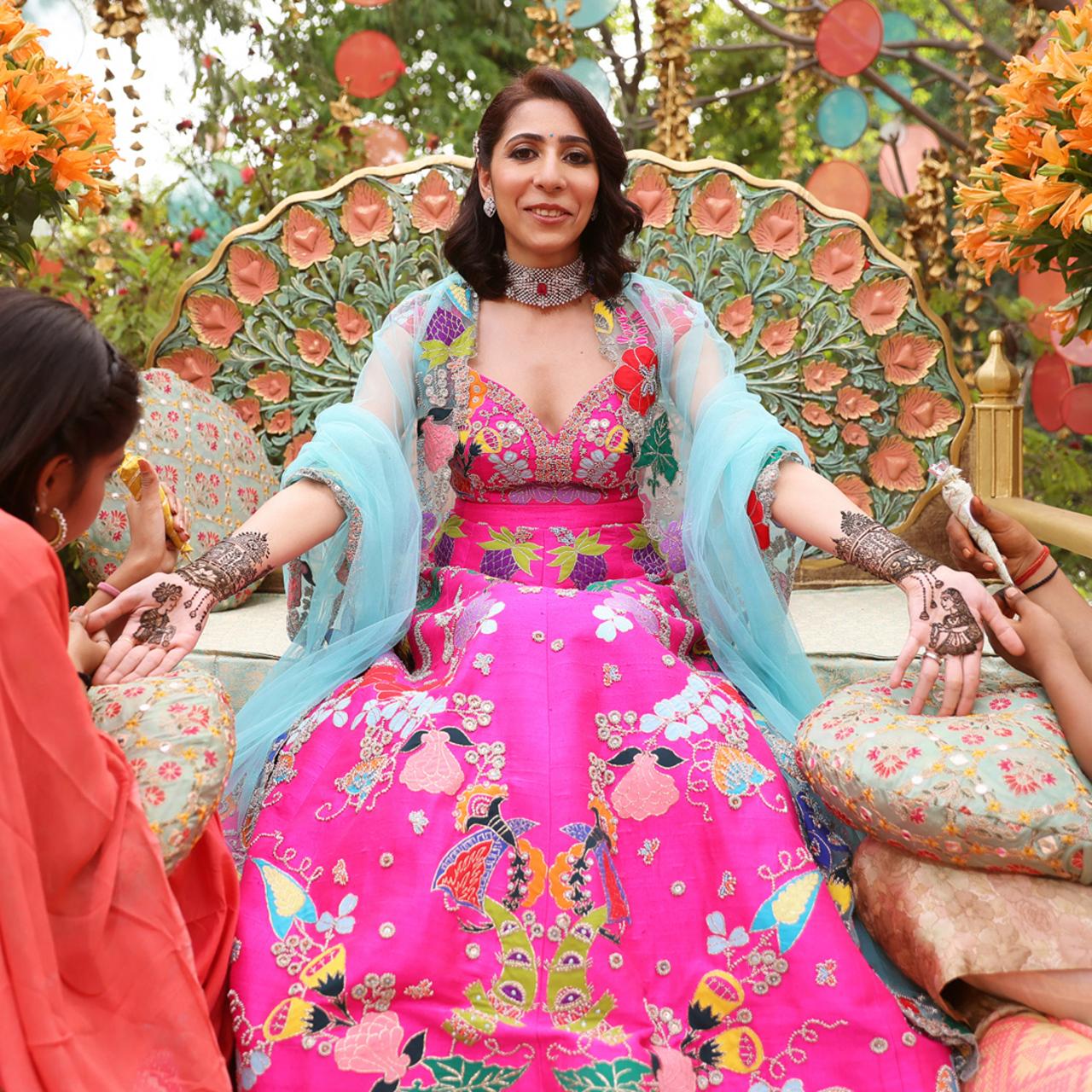Literally a goddess seated on a throne! Naina Sareen looks nothing less than divine in her long-flowing lehenga with vibrant colours and patterns. Don't forget her blue capri that trails off of her arms just above her mehendi