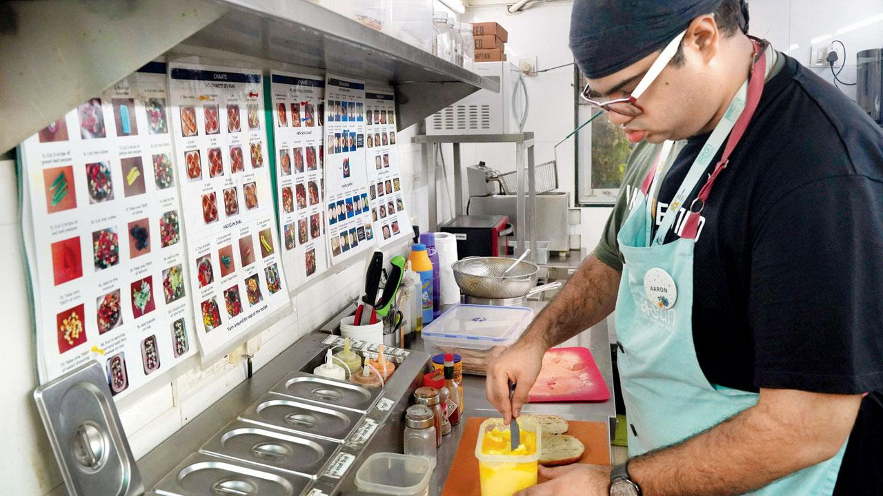 Chef Aaron prepares a sandwich. The food and recipe charts on the wall that the chef can memorise after just one read