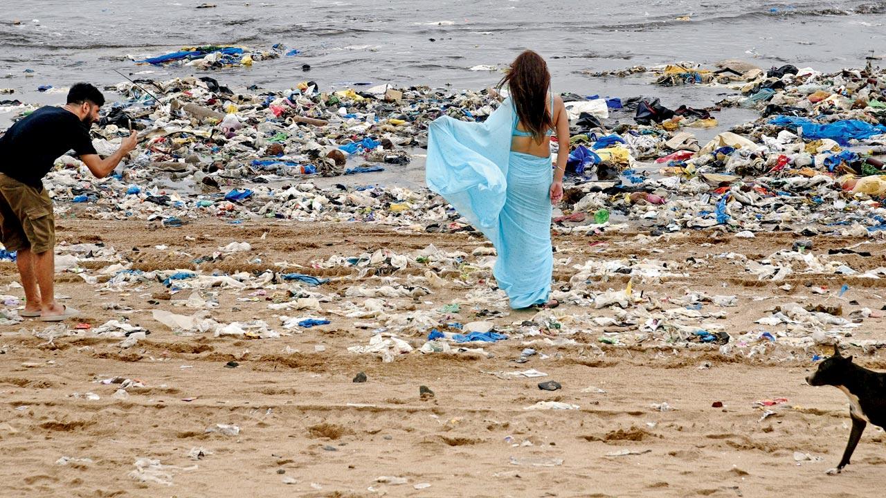 A woman poses amidst the garbage that has washed up at Versova beach while her companion takes a photo. Pic/Atul Kamble
