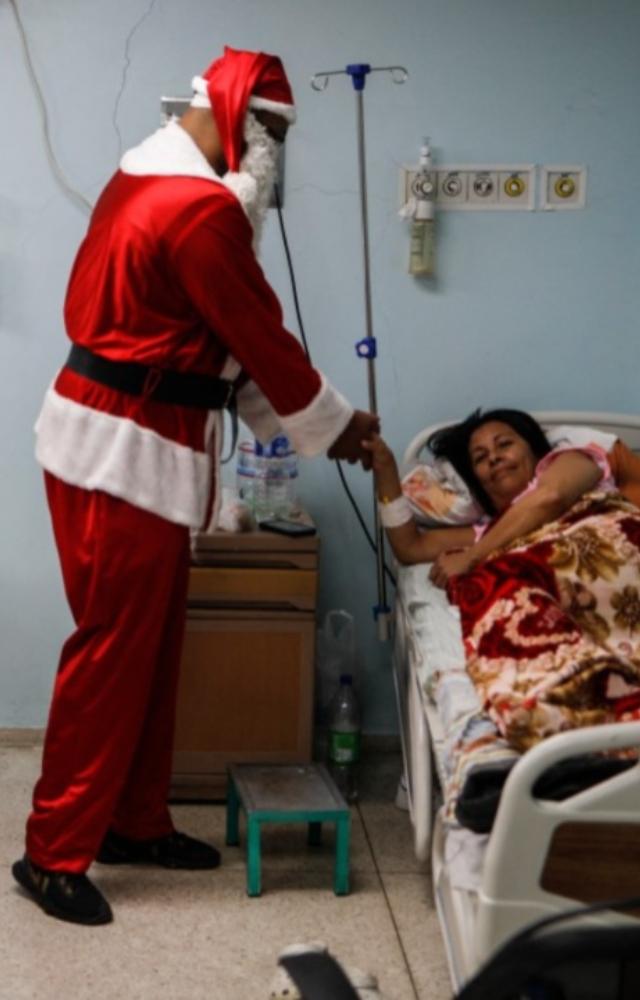 A man dressed as Santa Claus delivers a gift to a hospitalized woman in the emergency room of a hospital in the El Cementerio neighborhood of Caracas