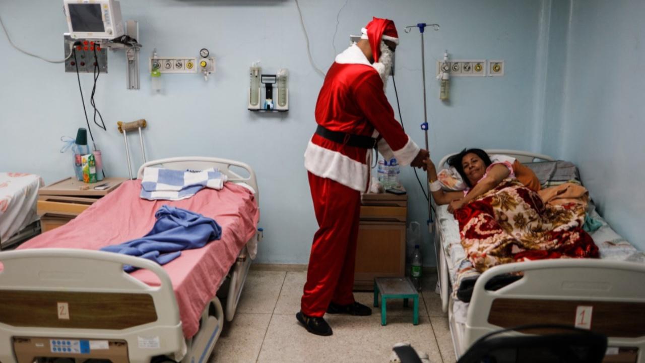 A man dressed as Santa Claus delivers a gift to a hospitalized woman in the emergency room of a hospital in the El Cementerio neighborhood of Caracas on December 25, 2023. This initiative by a group of volunteers from the San Miguel Arcangel Church of the El Cementerio neighborhood seeks to bring joy and hope to hospitalized children in a community facing economic difficulties. (Photo by Pedro Rances Mattey/AFP)