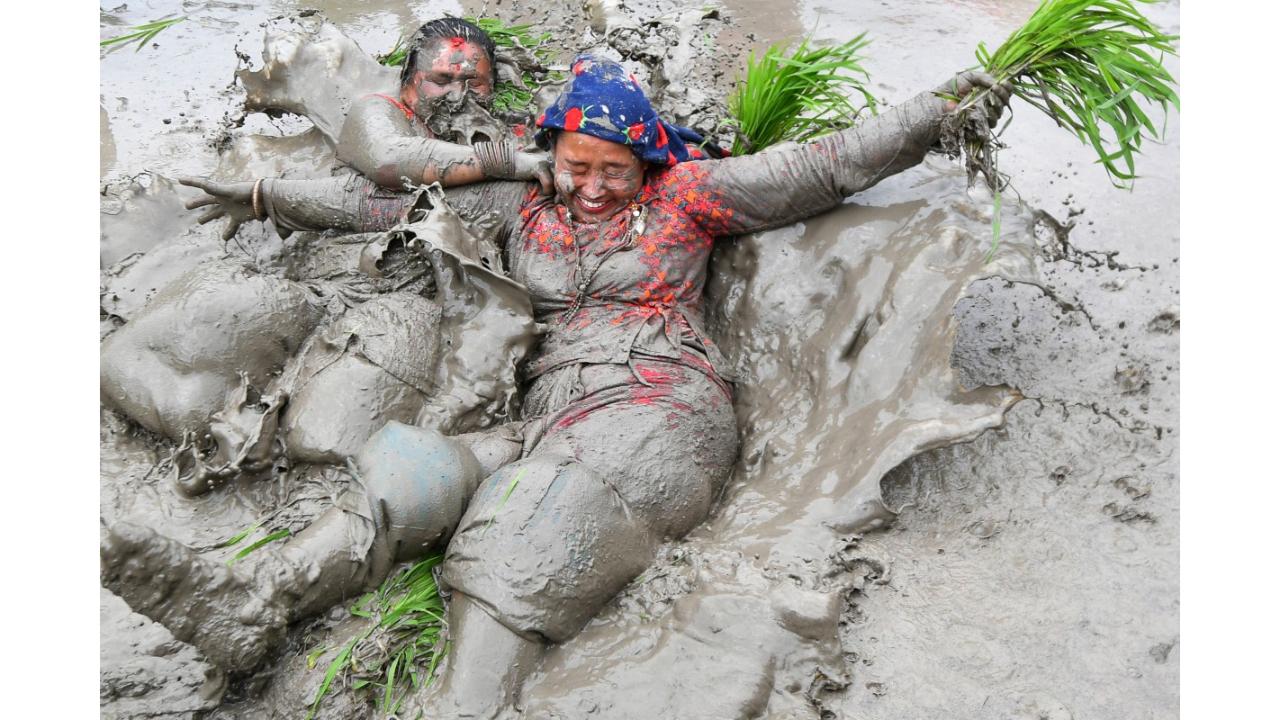 Mud-covered farmers play in a paddy field during 