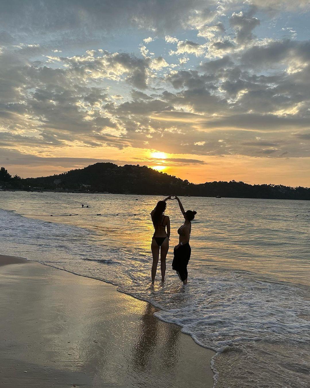 This one is a beautiful photo of Mouni and Disha by the beach during sunset, making a heart with their hands