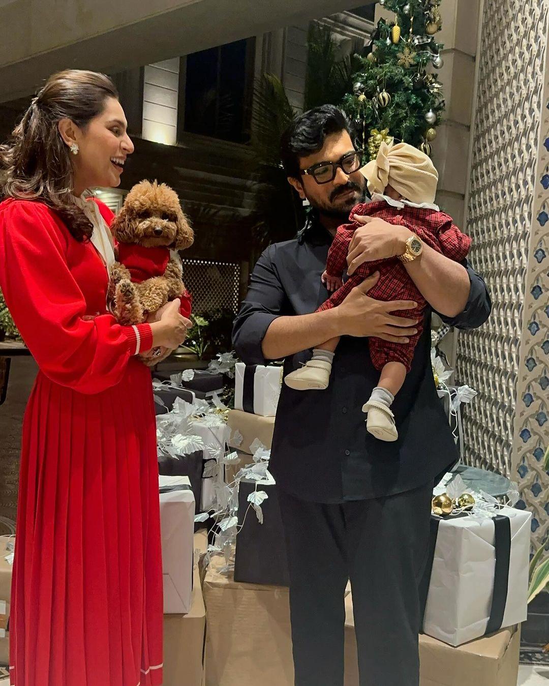 In the picture, Ram holds Klin Kaara in his arms, gazing at her with pure admiration and love. Upasana, dressed in a captivating red dress, complements Ram's dapper look in a crisp black shirt. Klin Kaara steals the show in a plaid Christmas onesie paired with a stylish head wrap.