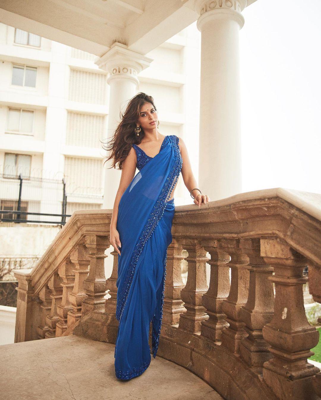 Suhana's electric blue chiffon saree is custom-designed and adorned with detailed mirror embellishments, cutdana embroidery showcasing intricate floral patterns, and beaded tassels enhancing the saree's beauty.