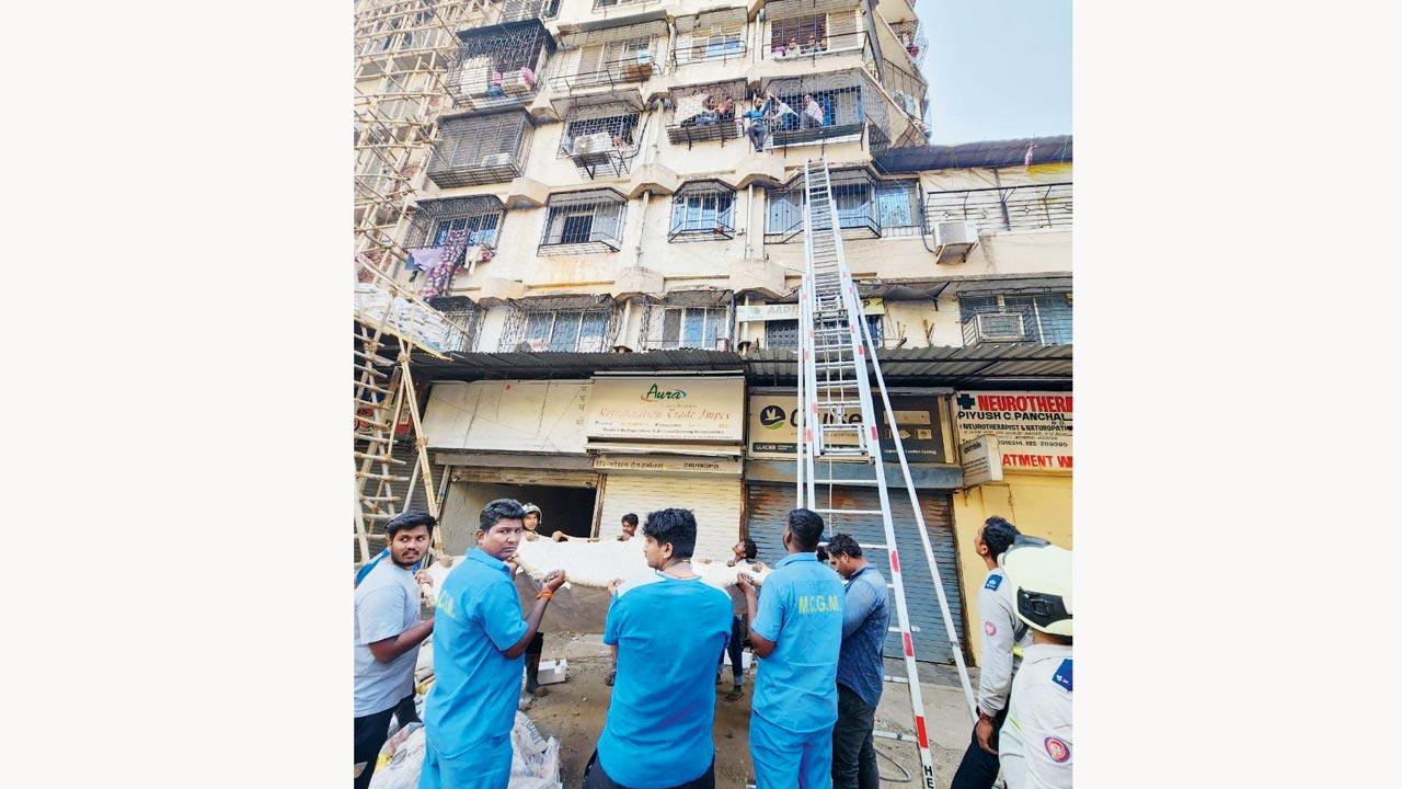 A team of rescuers patiently waits in the compound of the building, holding a sheet in case the man jumped