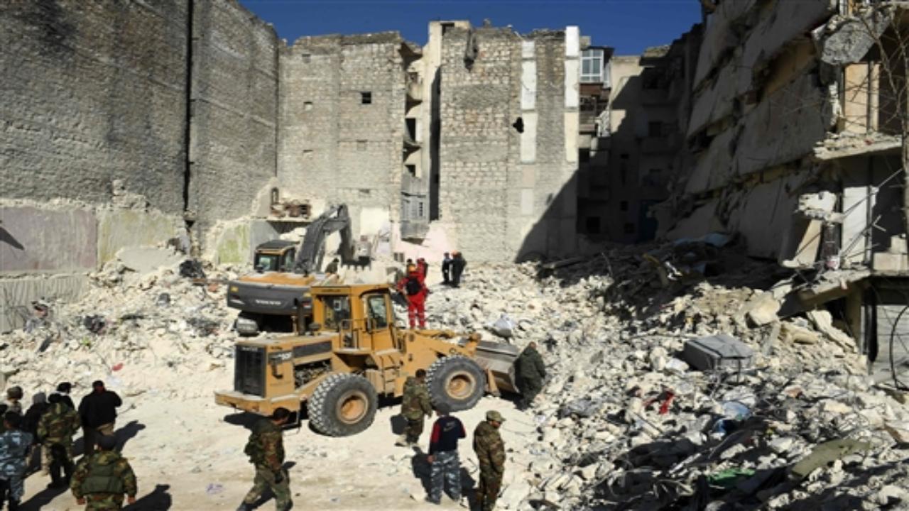 Syrian soldiers look on as rescuers use heavy machinery to sift through the rubble of a collapsed building in the northern city of Aleppo. Photo by AFP