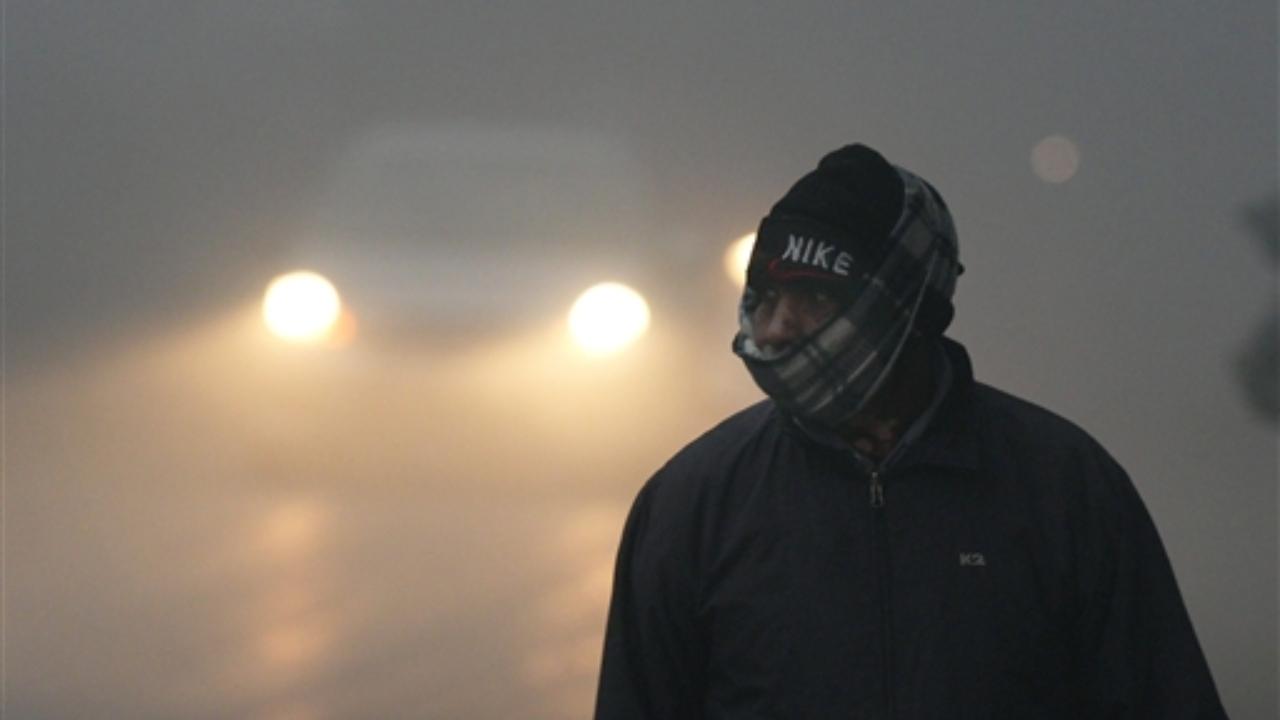 A pedestrian wearing woolens amid low visibility due to a thick layer of fog on a cold winter morning, in New Delhi