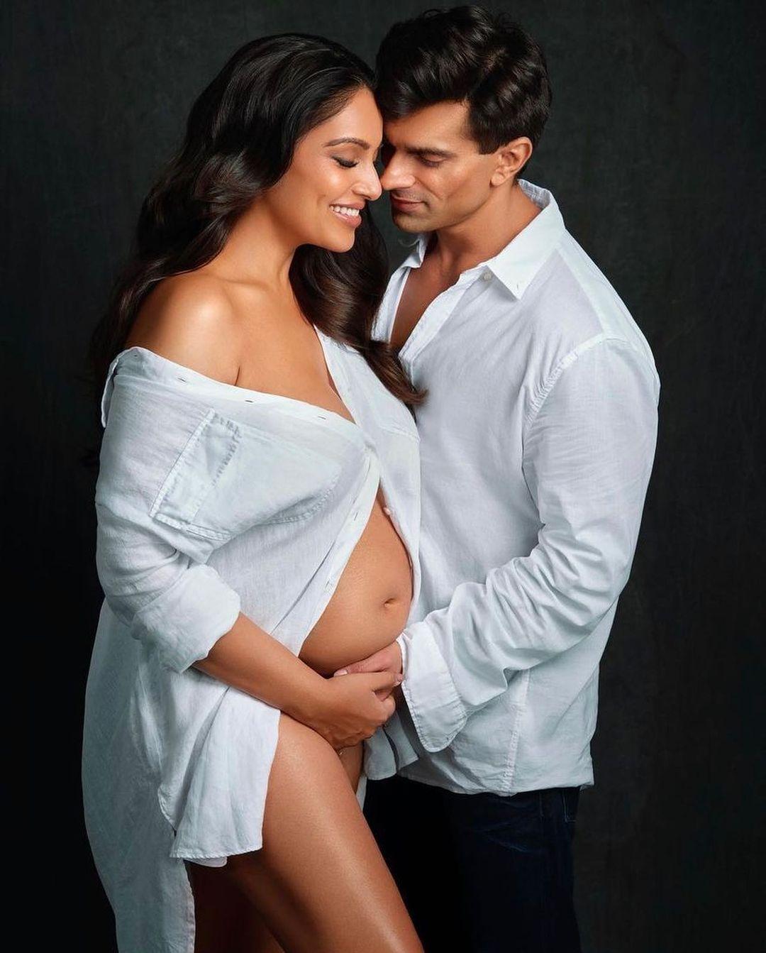 Clad in a shirt tastefully left unbuttoned to reveal her glowing bump, Bipasha radiates pure joy, while her husband's tender gaze reflects their shared excitement.