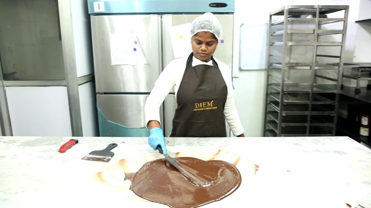 In this method of tempering chocolate, the chef breaks the chocolate into small pieces to prepare it for melting. It is stirred gently with a spatula while melting to ensure no lumps remain