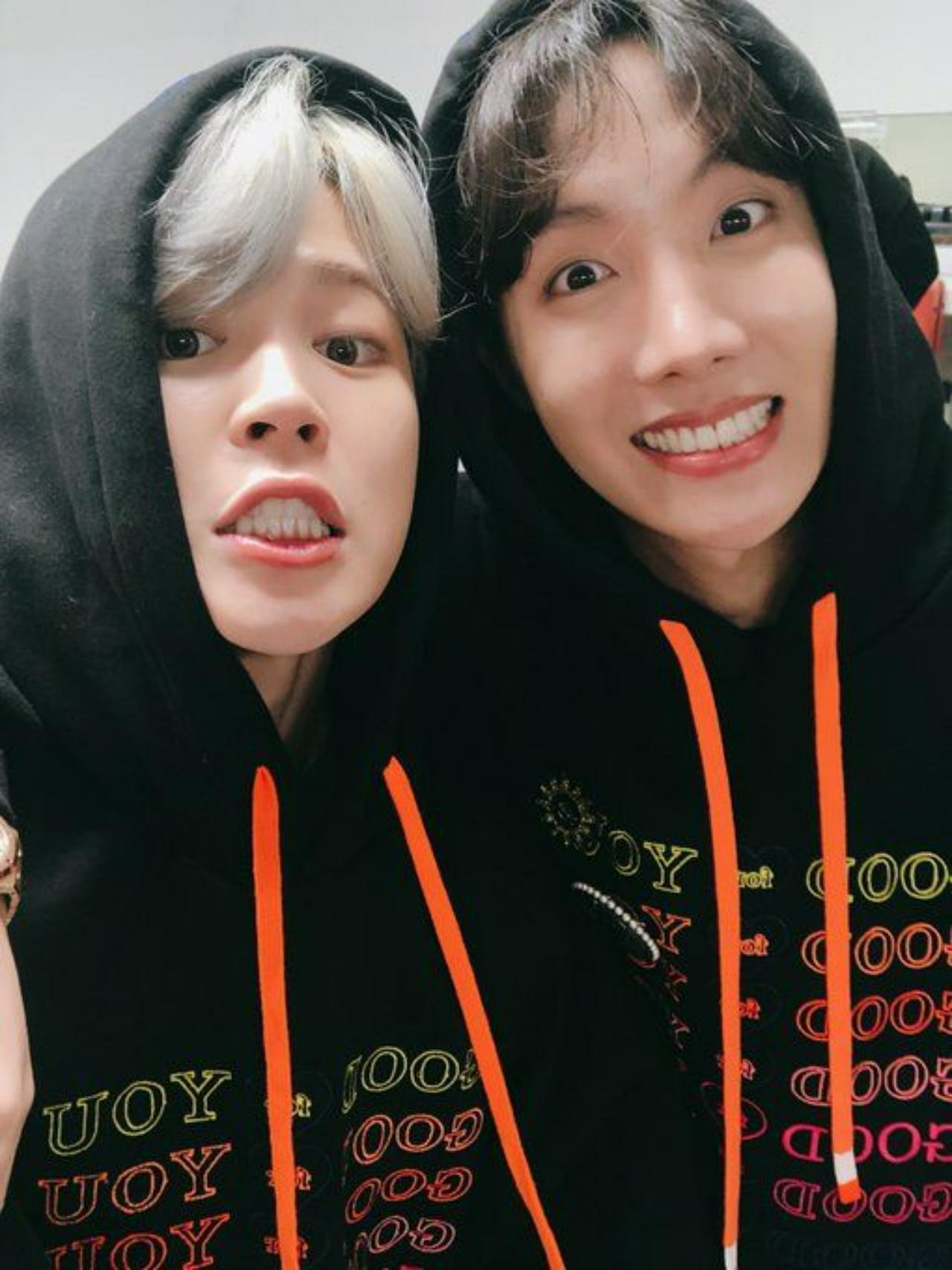 Jimin pulls his roommate Hobi hyung (J-Hope) in for a selfie as they twin in their black and orange hoodies