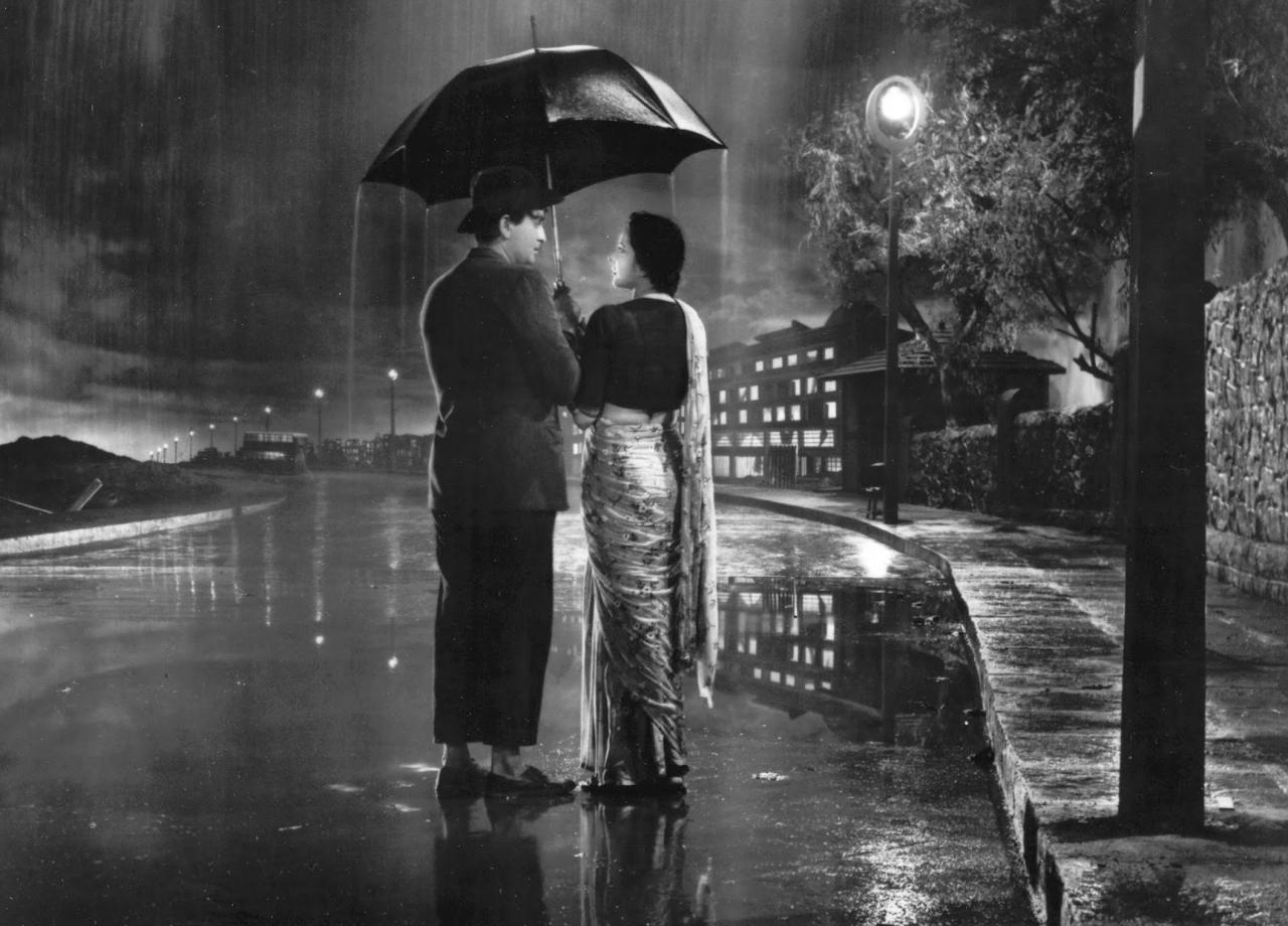Shree 420
'Shree 420' introduces us to a quirky character named Raj, clad in a laughable bowler hat and mismatched trousers. He arrives in Bombay with aspirations of employment, but experiences the harsh reality of city life when he is robbed just moments after stepping onto its sullied streets. However, he quickly learns that the true crooks in this city don tailored suits and perpetrate their illegal activities within their pretentious and fancy offices