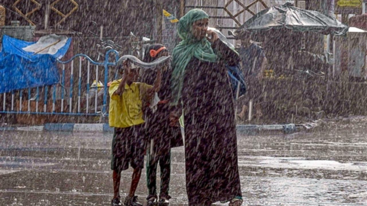 In Pic: A woman with school children crosses a road amid rains
 