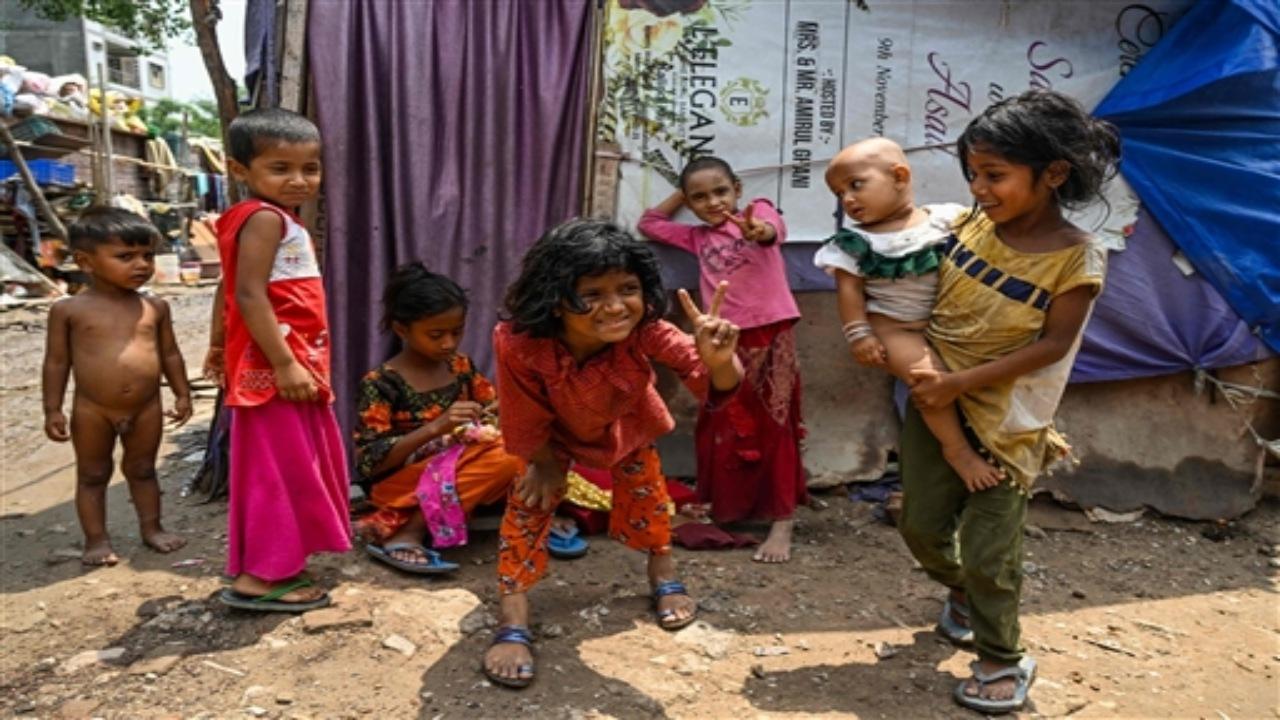 Rohingya refugee children gesture as they stand along a street at a refugee camp on the World Refugee Day, in New Delhi on June 20, 2023. 