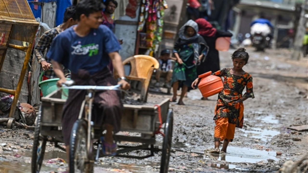 A Rohingya refugee girl gestures as she walks through a muddy street at a refugee camp on the World Refugee Day, in New Delhi on June 20, 2023. 