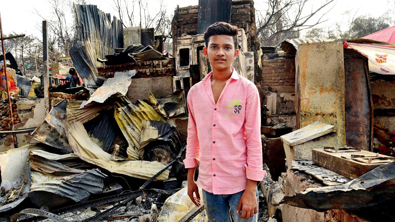 SSC examinee Aniket Ingale stands amid the charred remains of Anand Nagar slum in Malad East’s Appa pada on Tuesday. Pics/Nimesh Dave