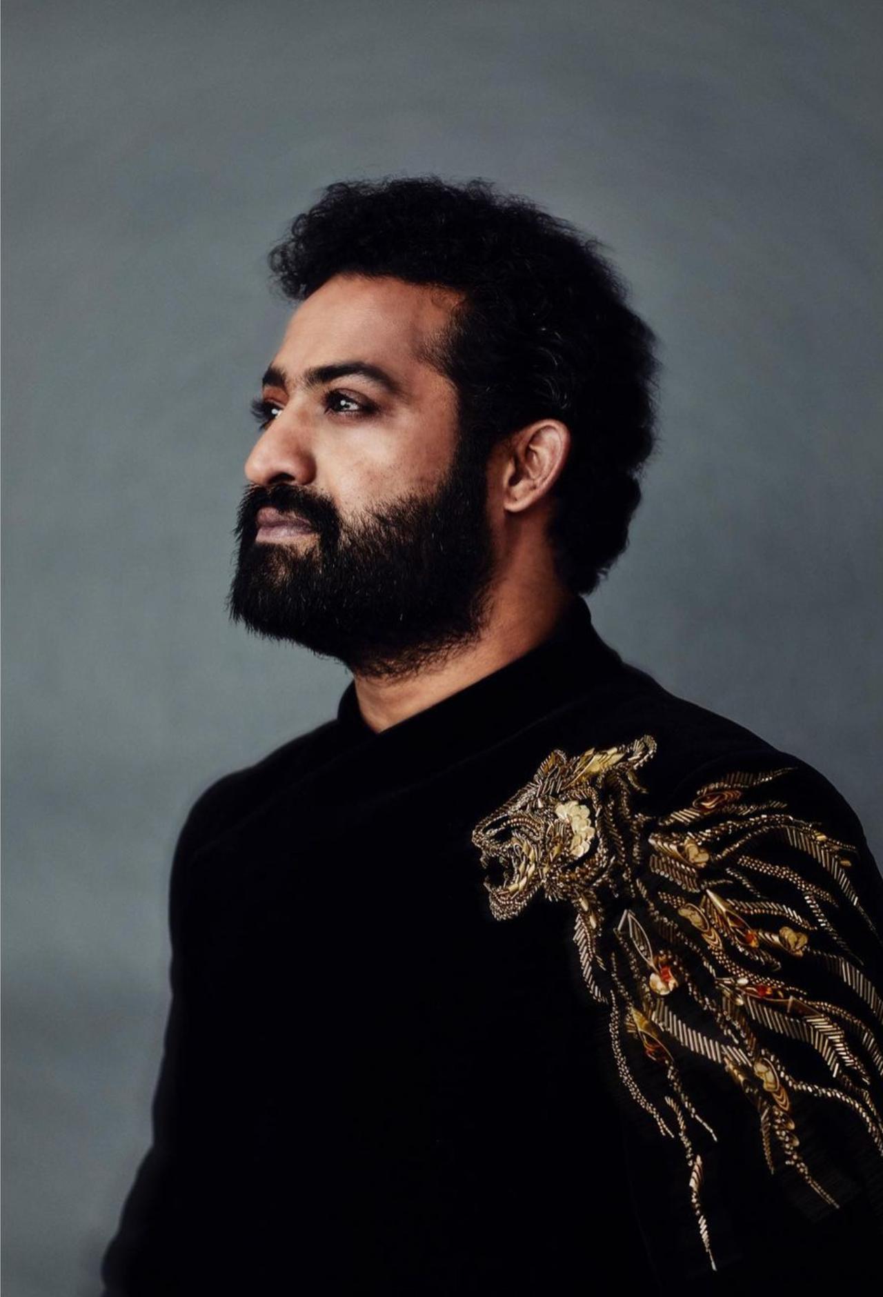 Jr NTR'S black velvet custom-made bandhgala with gold metallic embroidery by Indian fashion designer Gaurav Gupta. The delicate gold embroidery on the black velvet traditional bandhgala drew parallels to the national animal of India - The Tiger. It also is an ode to the iconic interval scene from RRR. And so befitting is this symbolic attire for The Young Tiger, a moniker popularly used for NTR Jr. The outfit was custom made for the global Icon keeping his sentiments in mind. The bandhgala was paired with Brue & Bareskin leather shoes and a Vacheron Constantin watch.