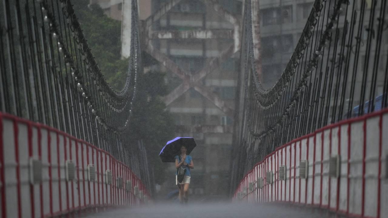 A woman uses an umbrella to shield herself from the rain as she walks along a suspension bridge in New Taipei City as typhoon Mawar approaches on the east coast.
