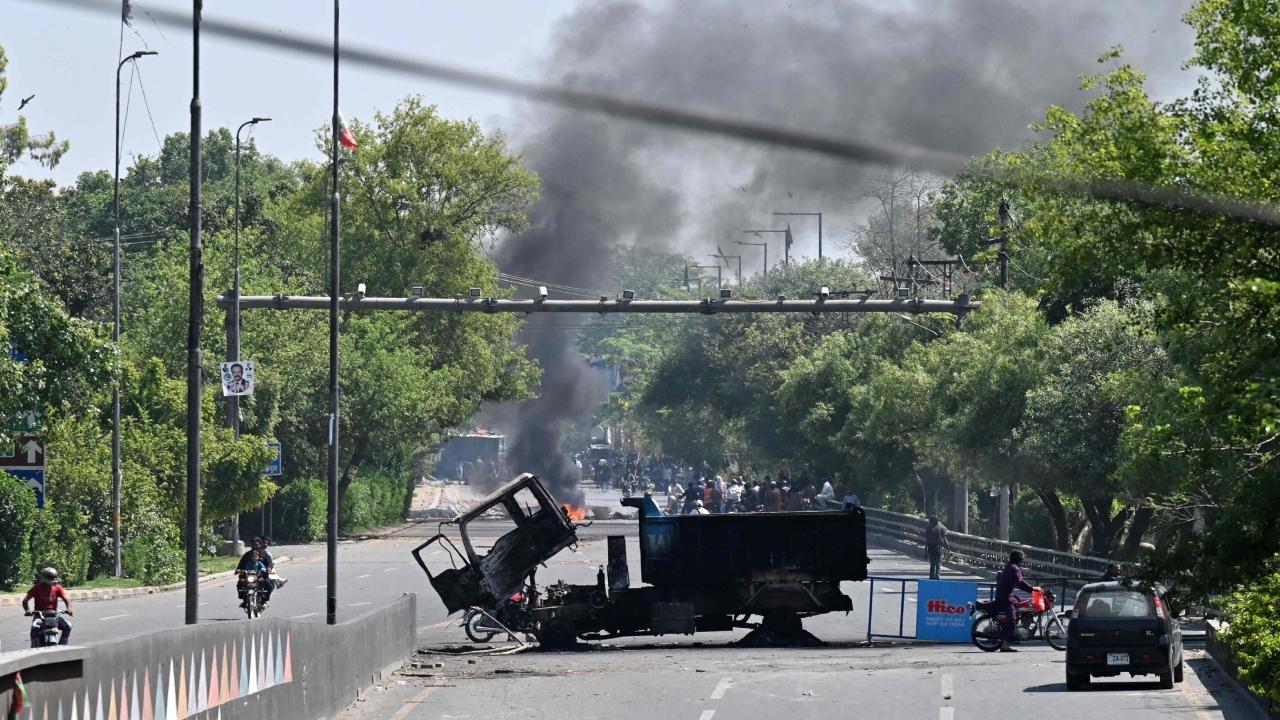 Motorists ride past burnt vehicles in front of the Zaman Park, a day after protests by Pakistan Tehreek-e-Insaf (PTI) party activists and supporters of former Pakistan's Prime Minister Imran Khan, in Lahore on May 10