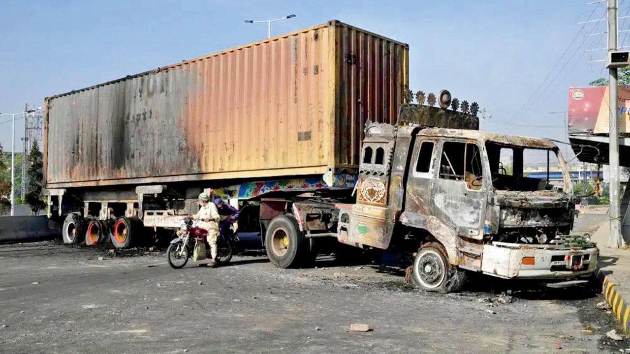 A motorcyclist passes through a truck burnt during clashes. Pic/AP