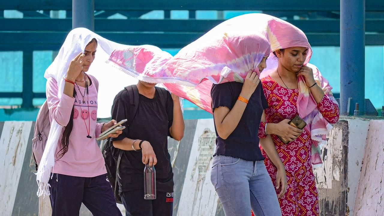 Commuters cover themselves with a scarf as they walk on a road during a hot summer day, in Gurugram, Saturday. Pic/PTI