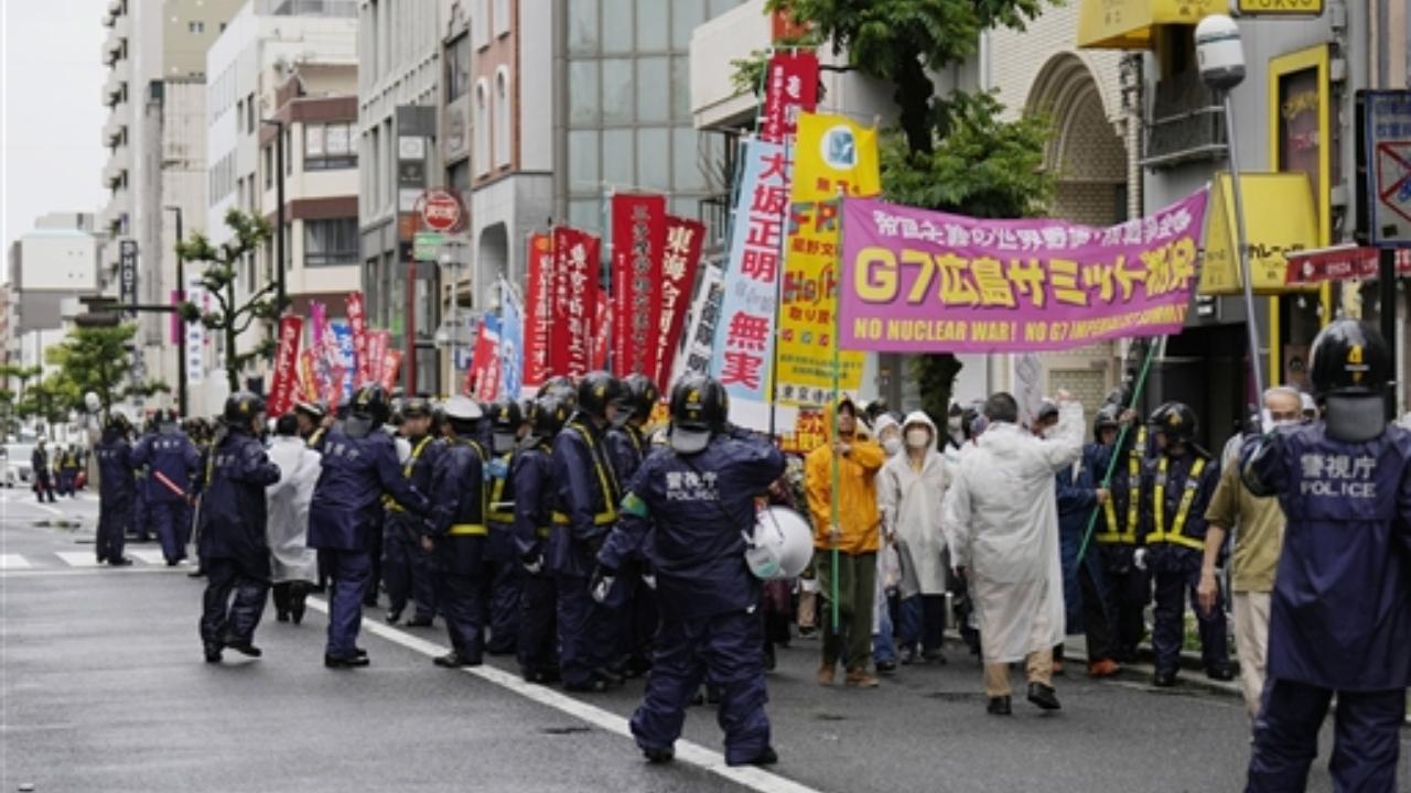 Police officers walk beside protesters chanting against the Group of Seven nations' meetings as they march on a street in Hiroshima