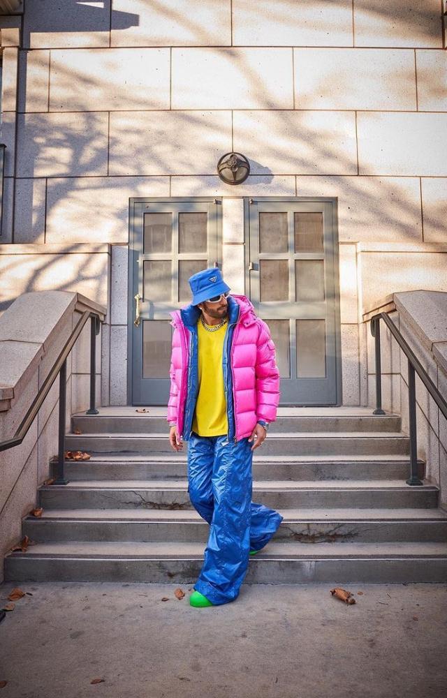 Pink puffer over a blue paired with a yellow t-shirt with blue bell bottoms, adding neon green shoes, white clout glasses, and a blue rain cap.