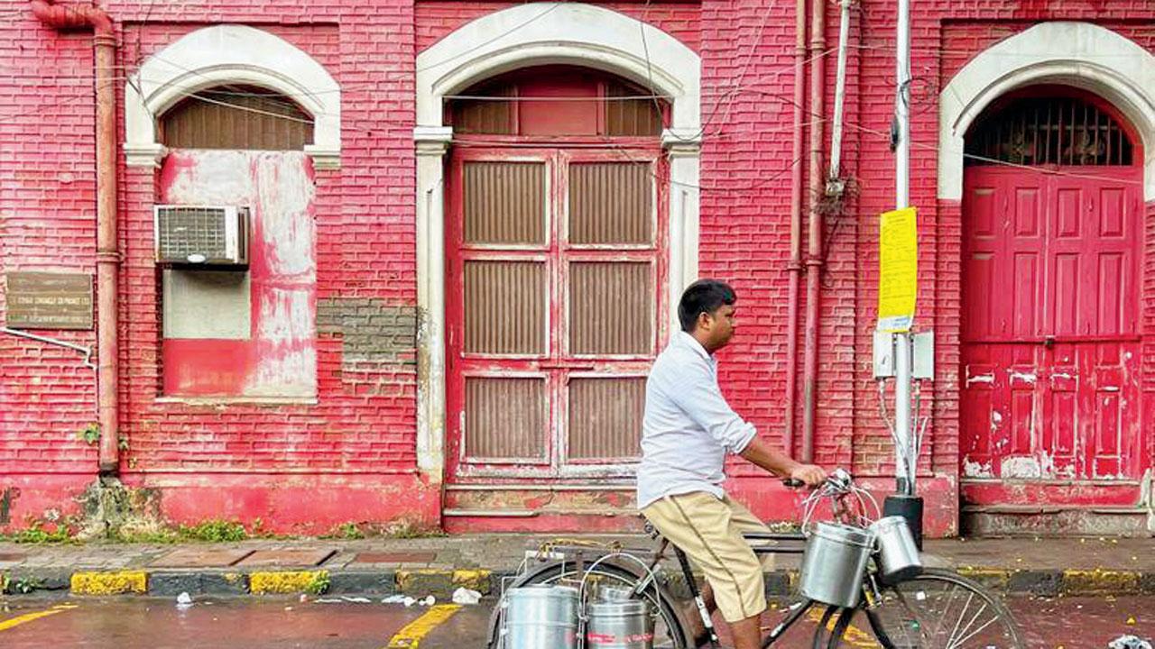 A photograph shows a dabbawala cycling near the Bombay Samachar building 