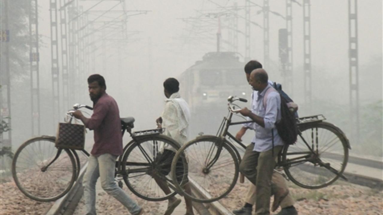 Commuters cross railway tracks amid low visibility due to smog, in Gurugram