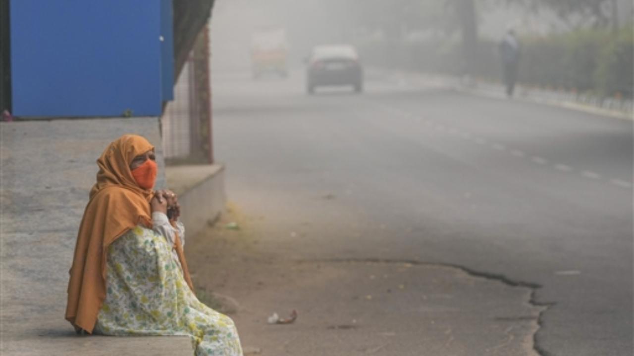 An elderly woman sits on a pavement during a smoggy morning