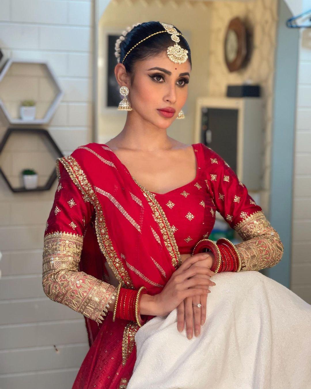 Mouni Roy's outfit choice, a stunning red lehenga with intricate golden designs and a graceful dupatta, is more than just a fashion statement – it's the perfect choice for Dashami. The detailed zari work on her blouse, along with the small embellishments, beautifully focuses on tradition.