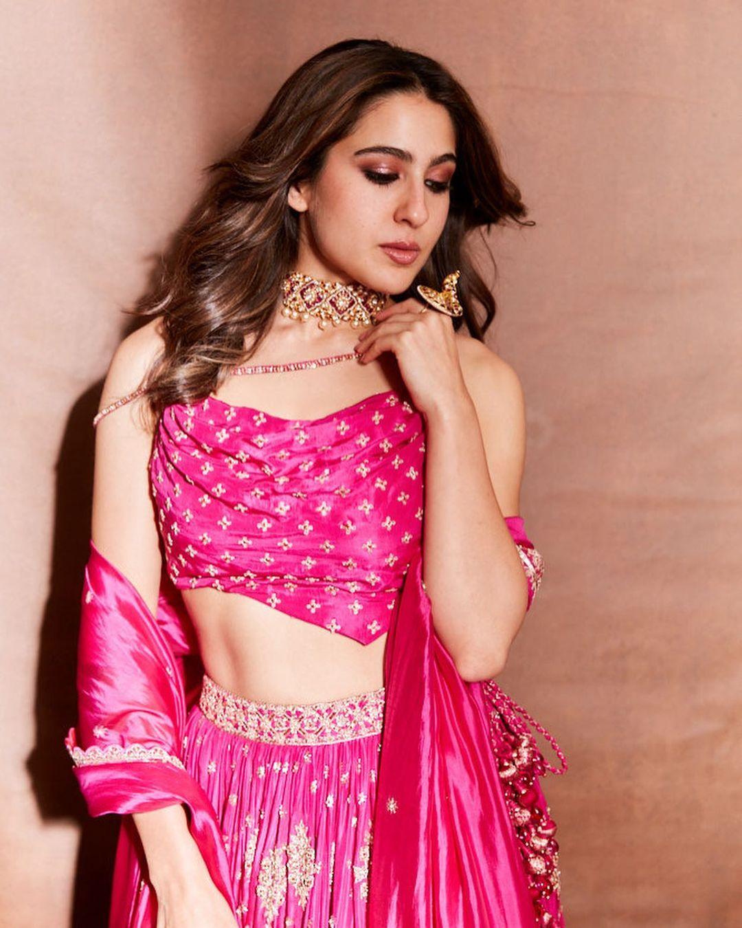 Her outfit includes a stunning pink slip blouse with an asymmetrical hem that beautifully showcases her toned abs. She perfectly pairs it with a gold and pink embroidered lehenga, and a silk rani pink dupatta adds the finishing touch to her show-stopping ethnic look.