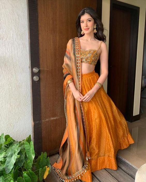 Shanaya Kapoor looked stunning in an outfit designed by Arpita Mehta. Her attire offered a unique twist on the classic look. It featured an orange skirt with a playful blurred polka dot pattern, paired with a tie-dye organza dupatta adorned with cowrie shell details. 