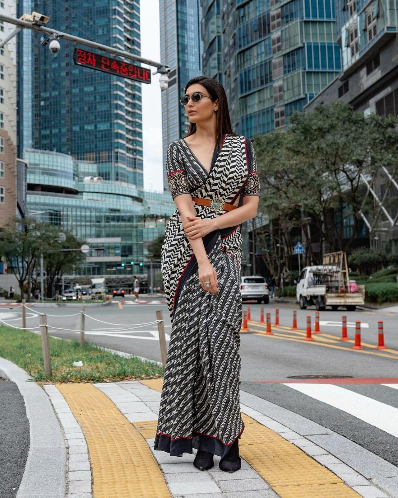 Karishma Tanna opted to add more black to her black-and-white saree look. She shared pictures of herself posing on the streets of Busan