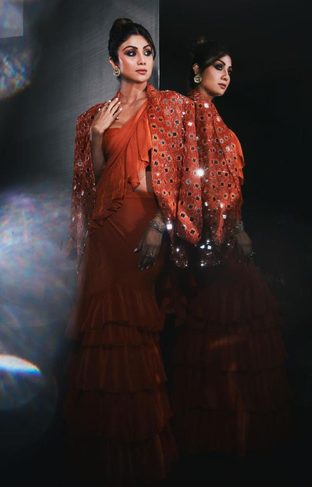 Shilpa Shetty looks gorgeous in an orange-colored saree with a mirror work jacket and tube blouse.