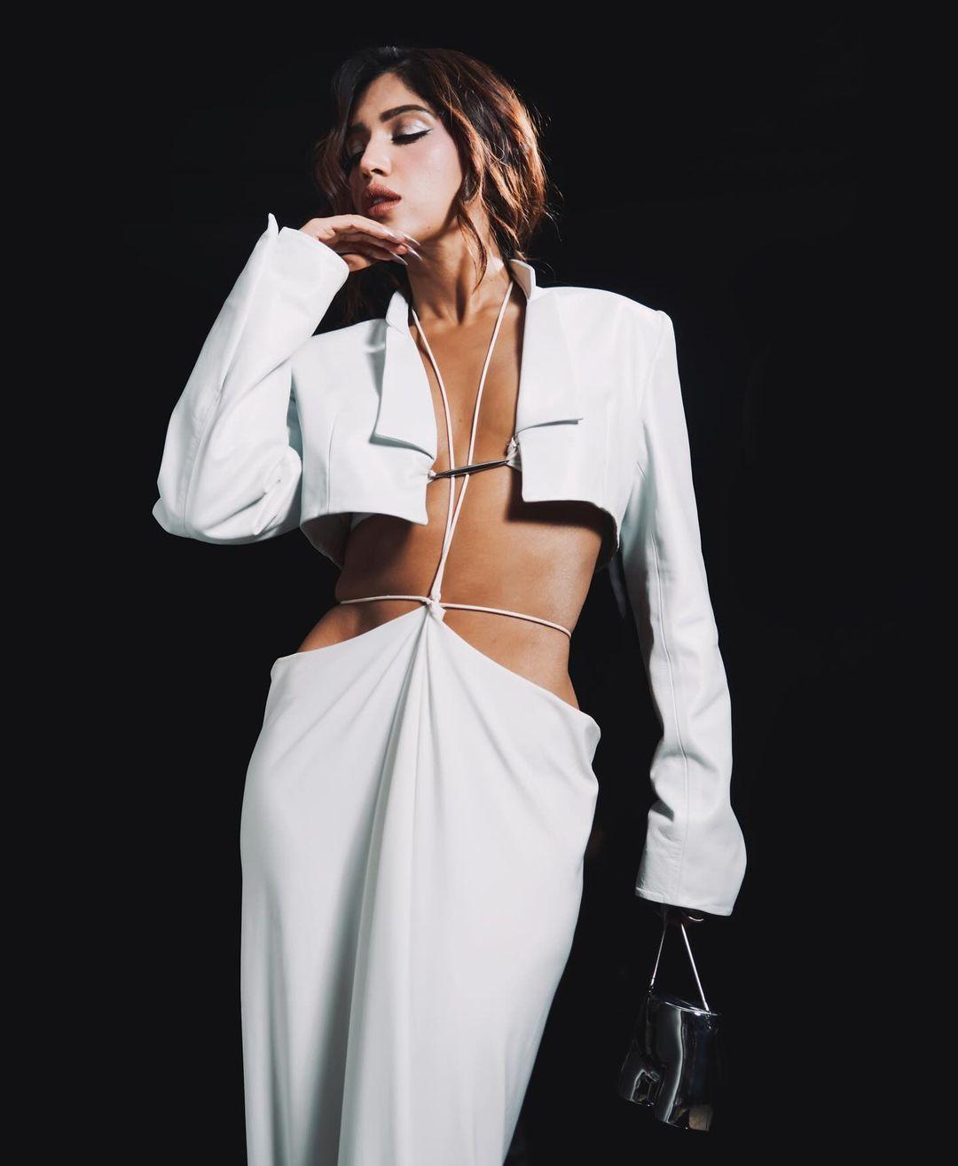She was photographed wearing a white ensemble that included a bralette top with metallic piping, a long skirt with a back plate held together by strings, and an unbuttoned cropped blazer.