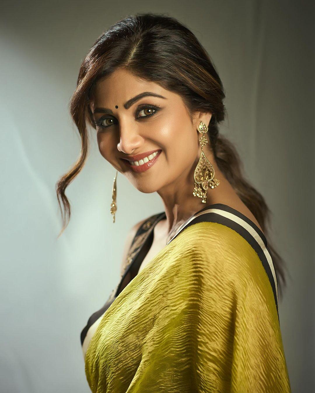 The saree features a lively mustard green colour on the pallu, with a bold black and white striped print at the bottom. Shilpa pairs it effortlessly with a black sleeveless blouse adorned with golden floral prints