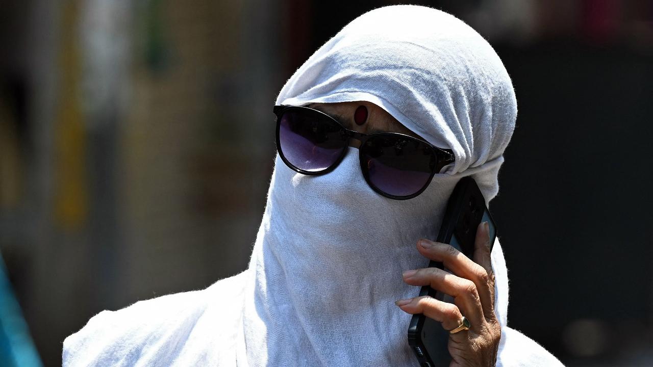 A woman with her face covered by cloth, speaks on a mobile phone amidst scorching heat (Photo by Noah SEELAM/AFP)