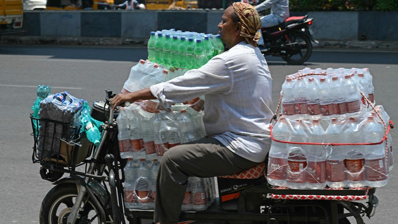 A worker transports water bottles on his two-wheeler during midday (Photo by Noah SEELAM/AFP)