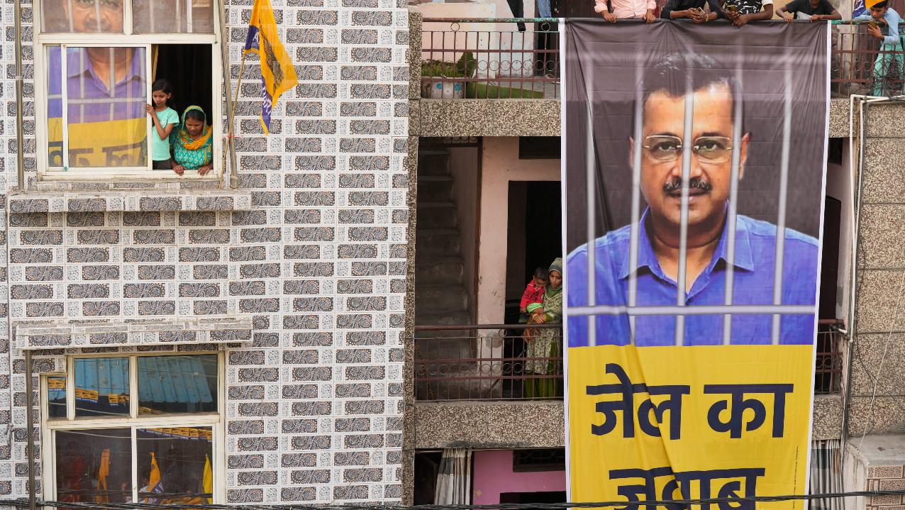 Locals watch as a large banner of jailed Delhi Chief Minister Arvind Kejriwal hangs from the balcony of a building during his wife Sunita Kejriwal’s election roadshow. Pic/PTI