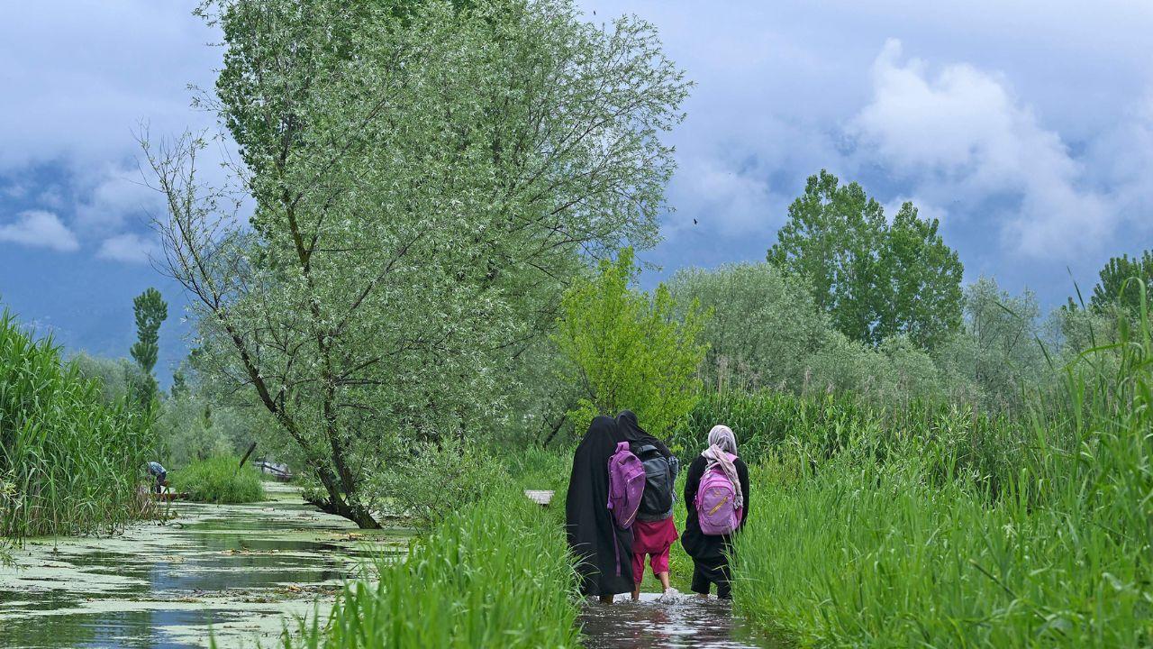 School children wade along a flooded path as water levels rose in the interior of Dal Lake due to heavy rains in Srinagar on April 30, 2024. (Photo by TAUSEEF MUSTAFA / AFP)