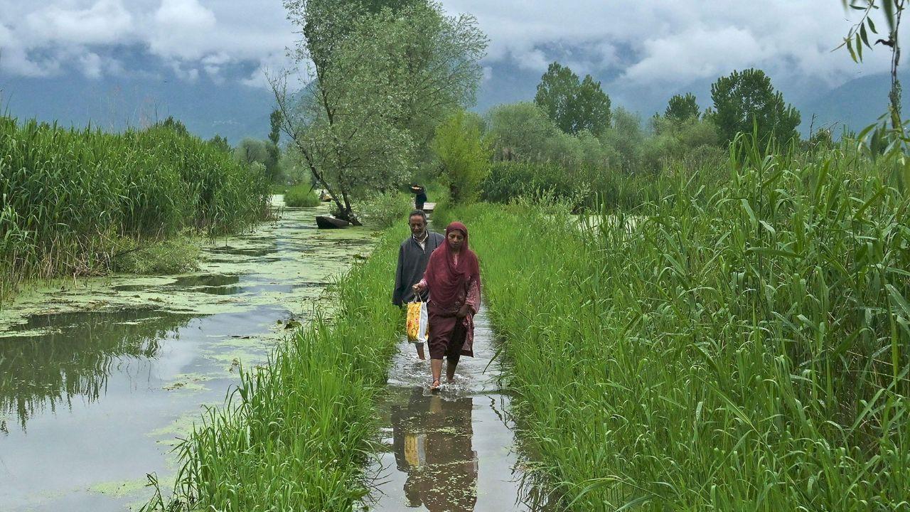 Residents wade along a flooded path next to a canal after water levels rose in the interior of Dal Lake due to heavy rains in Srinagar on April 30, 2024. (Photo by TAUSEEF MUSTAFA / AFP)