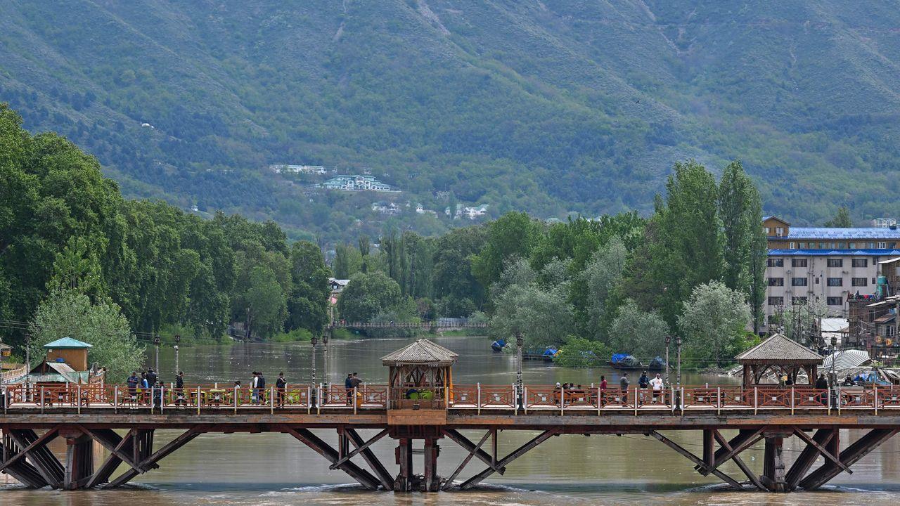 People walk across a bridge over the River Jehlum in Srinagar on April 30, 2024, following heavy rains that increased water levels. (Photo by TAUSEEF MUSTAFA / AFP)