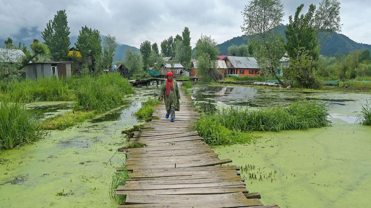 A woman walks along a wooden foot bridge after water levels rose in the interior of Dal Lake due to heavy rains in Srinagar on April 30, 2024. (Photo by TAUSEEF MUSTAFA / AFP)
